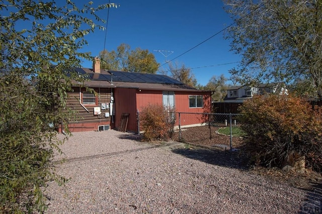 rear view of house featuring fence, a chimney, and solar panels