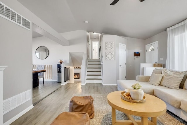 living room featuring visible vents, baseboards, stairs, a lit fireplace, and light wood-type flooring