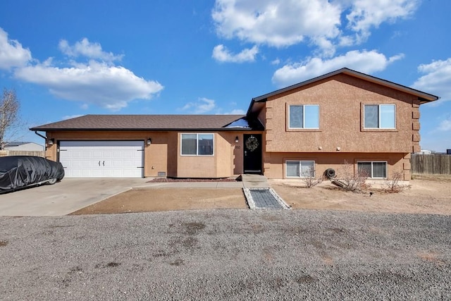 split level home with a garage, concrete driveway, fence, and stucco siding