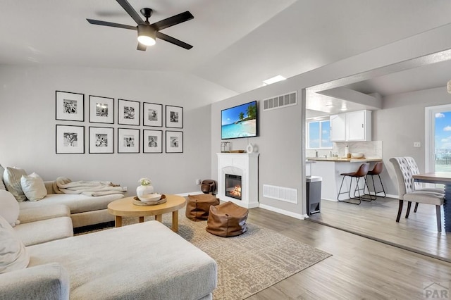 living area featuring lofted ceiling, visible vents, wood finished floors, and a glass covered fireplace