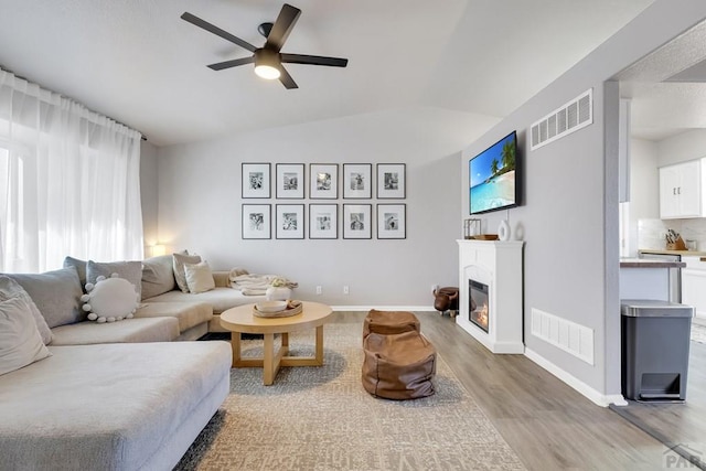 living area with lofted ceiling, wood finished floors, a glass covered fireplace, and visible vents