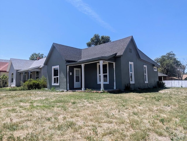 view of front of home with a front yard, roof with shingles, fence, and stucco siding