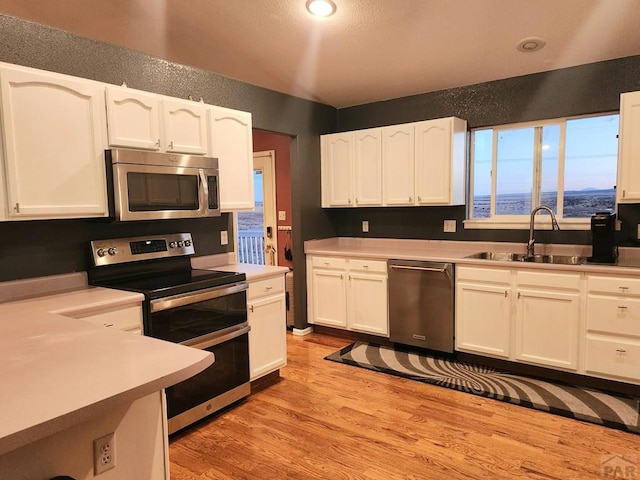 kitchen with light wood-style flooring, appliances with stainless steel finishes, white cabinets, and a sink