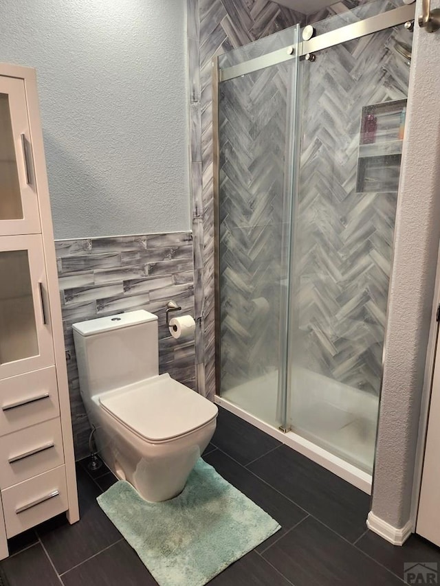 full bathroom with a stall shower, tile patterned flooring, a textured wall, and toilet