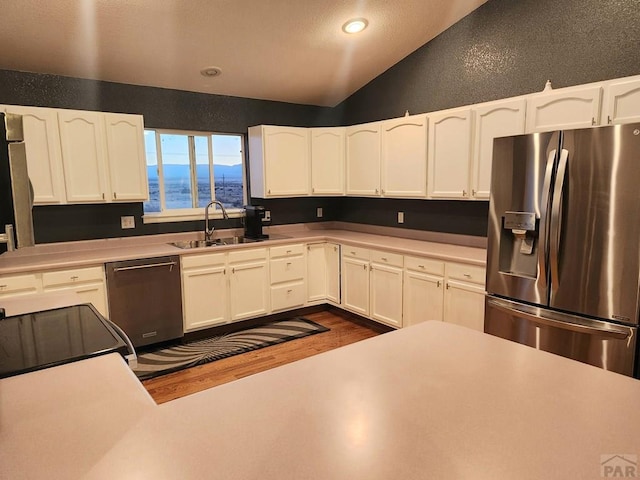 kitchen with a textured wall, appliances with stainless steel finishes, white cabinets, vaulted ceiling, and a sink