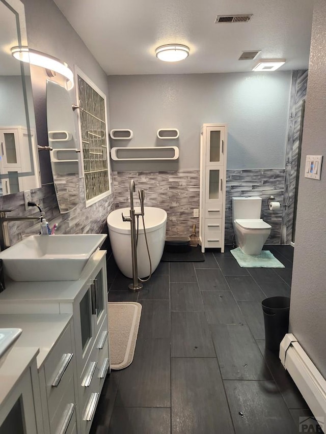 bathroom with a soaking tub, visible vents, baseboard heating, wainscoting, and vanity