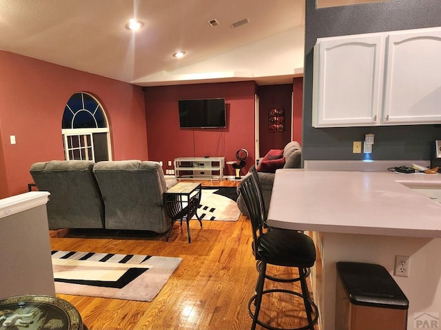 kitchen with light wood finished floors, a breakfast bar area, lofted ceiling, open floor plan, and white cabinetry