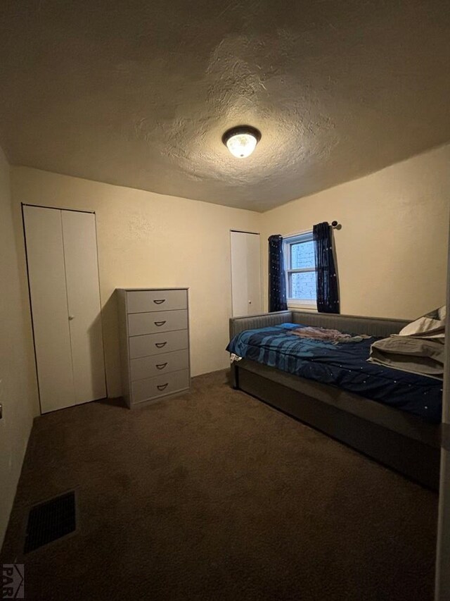 bedroom with a textured ceiling, dark carpet, and visible vents