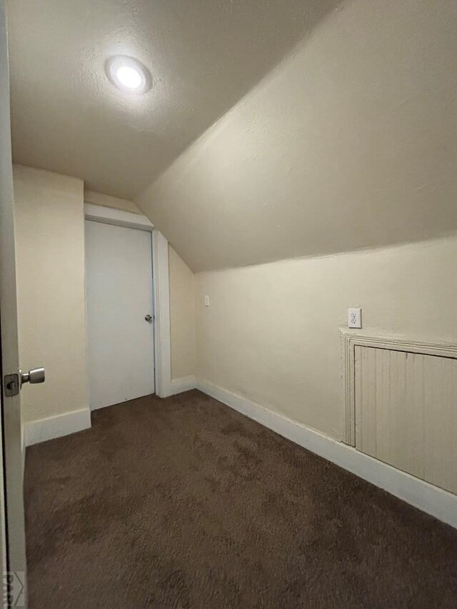 bonus room featuring vaulted ceiling, baseboards, dark colored carpet, and a textured ceiling