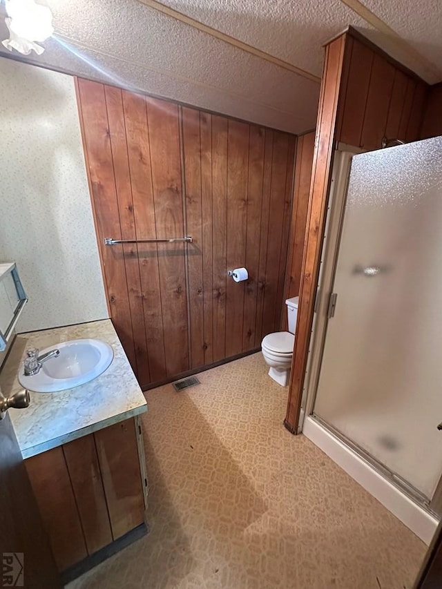 bathroom with vanity, a stall shower, toilet, wood walls, and visible vents