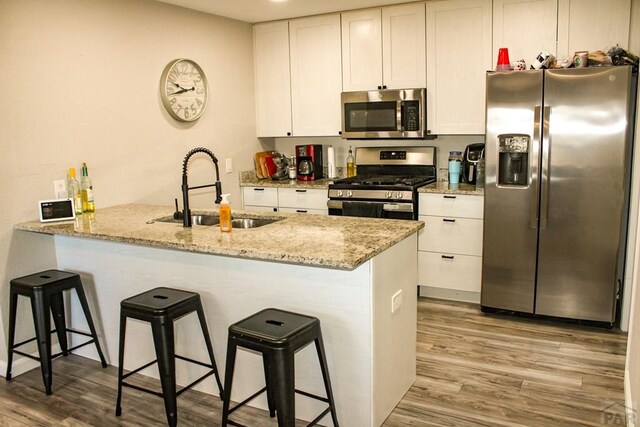 kitchen with stainless steel appliances, a peninsula, a sink, and white cabinetry