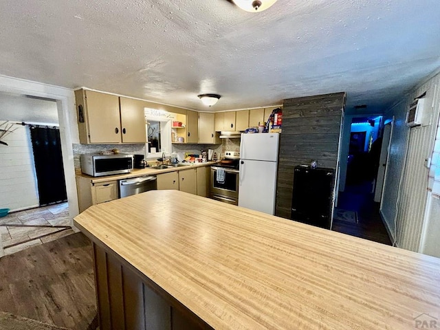 kitchen with wood finished floors, stainless steel appliances, a textured ceiling, light countertops, and a sink