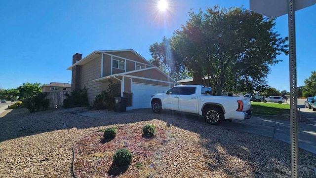 view of side of property with a garage, driveway, a chimney, and fence