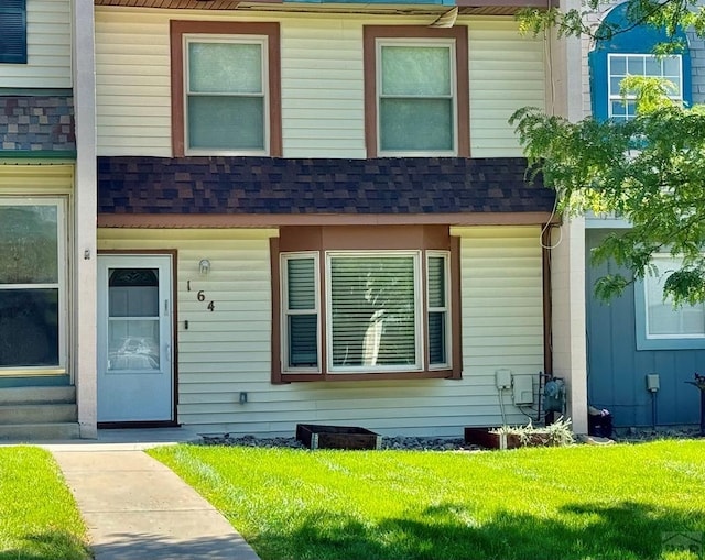 view of front of house featuring entry steps, a front lawn, roof with shingles, and mansard roof