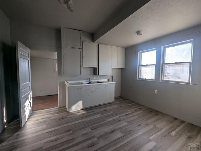 kitchen featuring light wood-style floors, white cabinetry, light countertops, and a sink