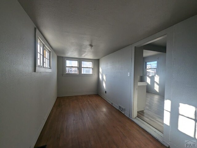 empty room with plenty of natural light, baseboards, dark wood finished floors, and a textured ceiling