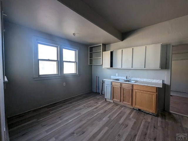 kitchen featuring brown cabinets, wood finished floors, a sink, light countertops, and beam ceiling