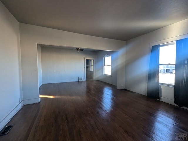 empty room with dark wood-type flooring, visible vents, and baseboards