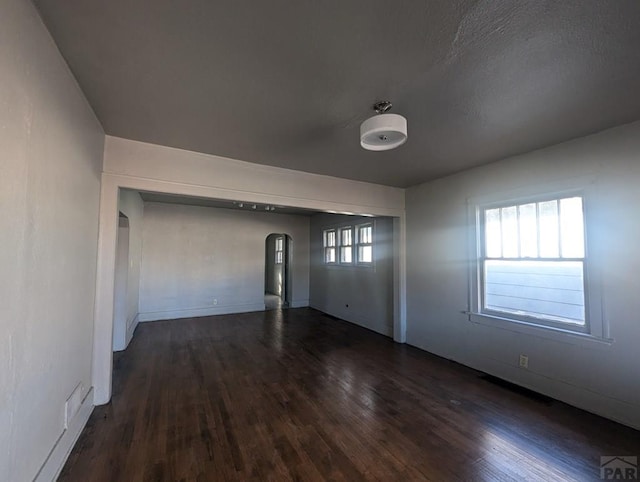 empty room featuring dark wood-style floors and arched walkways