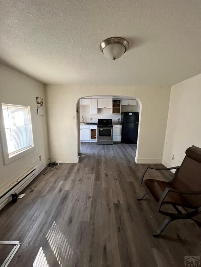 1434 E Evans Ave, Pueblo, CO 81004 - unfurnished living room featuring dark wood-type flooring, baseboards, a textured ceiling, and arched walkways