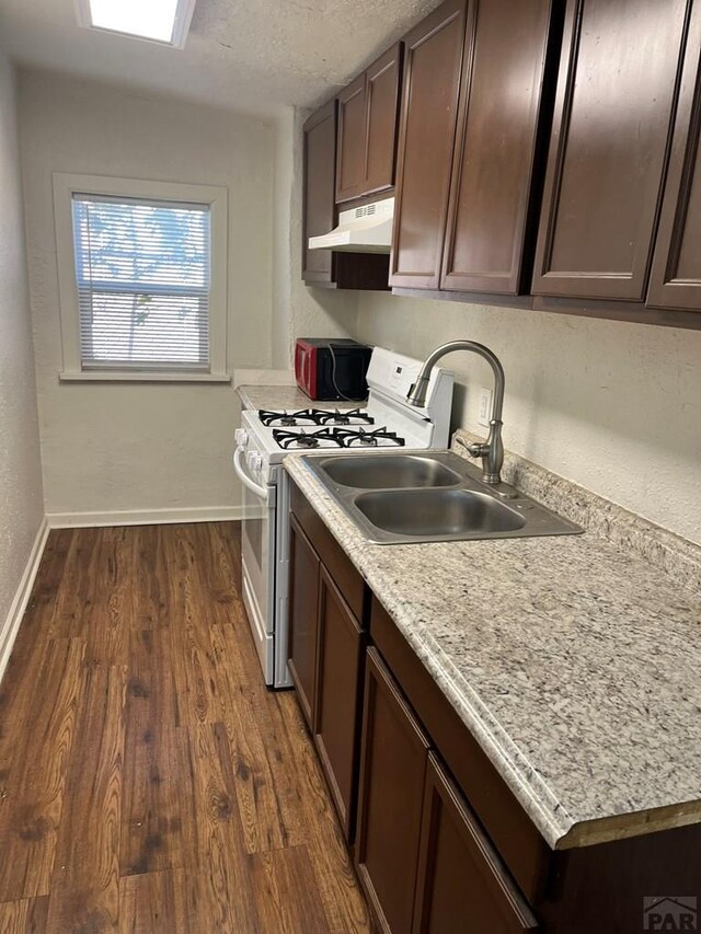 1434 E Evans Ave, Pueblo, CO 81004 - kitchen featuring white range with gas stovetop, baseboards, under cabinet range hood, and light countertops