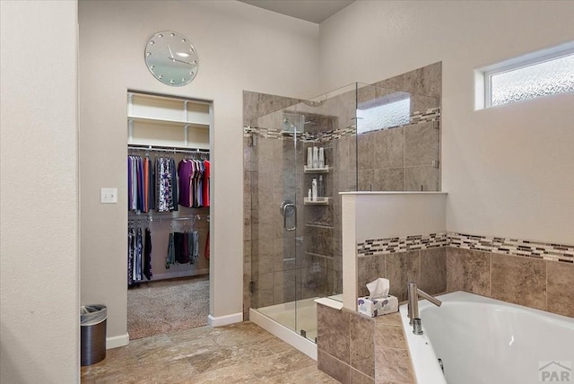 bathroom with baseboards, a spacious closet, a shower stall, and a bath