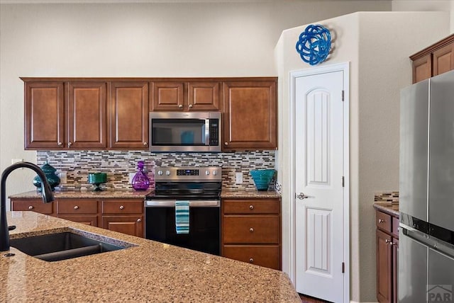 kitchen with appliances with stainless steel finishes, a sink, light stone counters, and tasteful backsplash