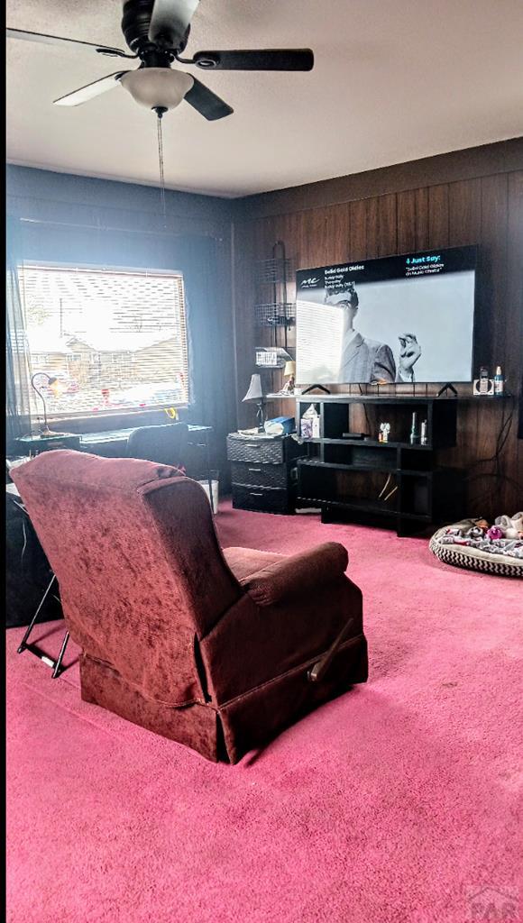 2318 W 17th St, Pueblo, CO 81003 - living room featuring carpet flooring, ceiling fan, healthy amount of natural light, and wood walls