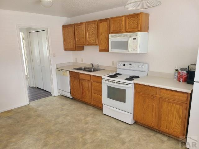 kitchen featuring light countertops, white appliances, brown cabinetry, and a sink