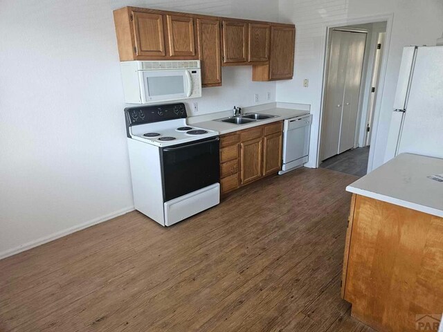 kitchen featuring dark wood-style flooring, light countertops, brown cabinetry, a sink, and white appliances