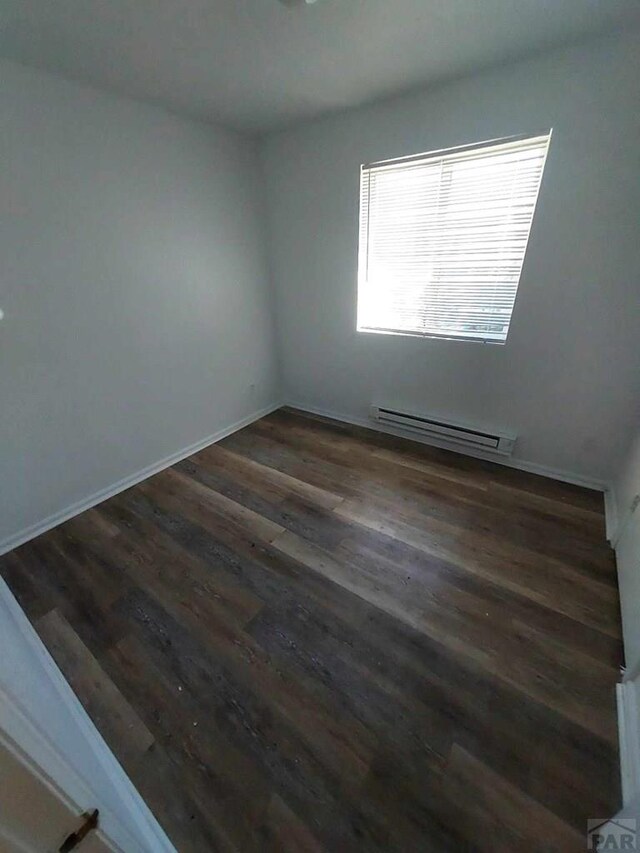 empty room with baseboards, dark wood finished floors, and baseboard heating