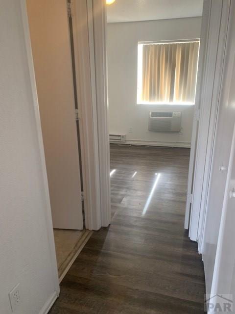 corridor with a baseboard heating unit, dark wood-style flooring, and a wall unit AC