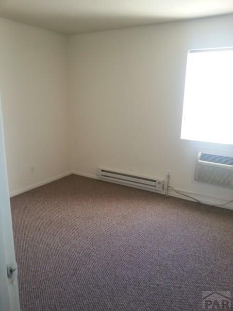 carpeted empty room with a baseboard heating unit and an AC wall unit