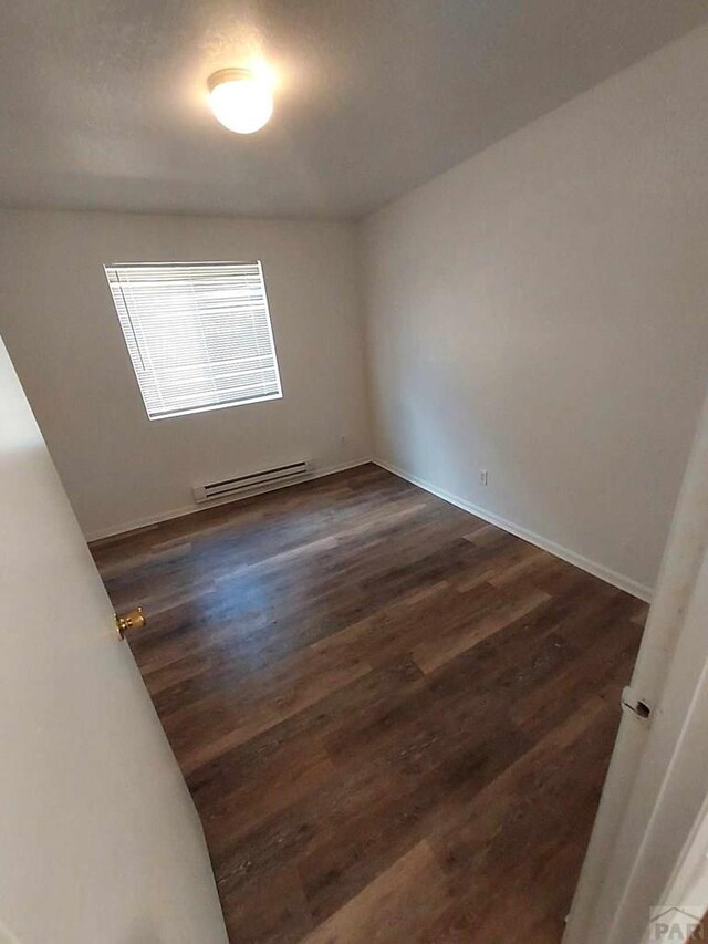 unfurnished room with a baseboard heating unit, dark wood-style flooring, and baseboards