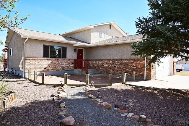 view of front of property with driveway, brick siding, an attached garage, and stucco siding