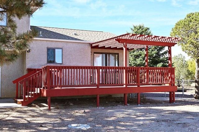 back of property with a shingled roof, stucco siding, a wooden deck, and a pergola