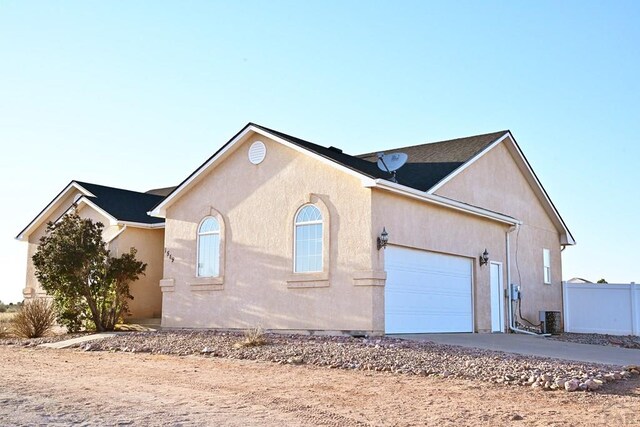 exterior space with a garage, central air condition unit, fence, and stucco siding