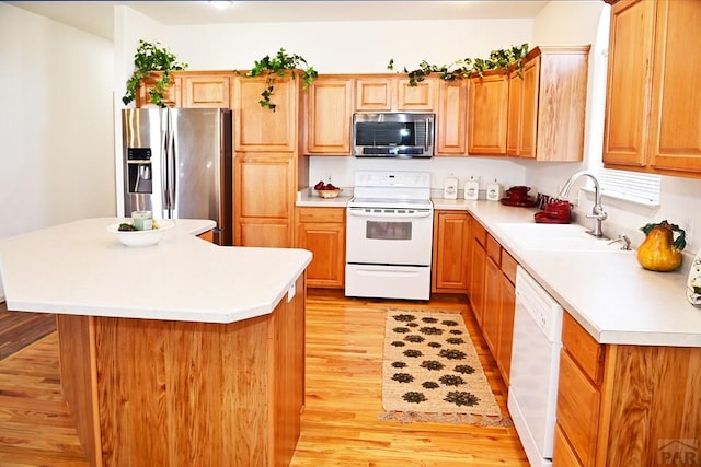 kitchen featuring light wood-style flooring, stainless steel appliances, a kitchen island, a sink, and light countertops