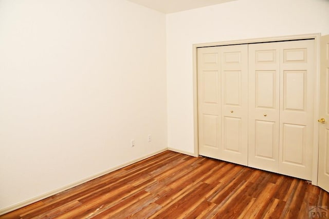 unfurnished bedroom featuring dark wood-style floors, baseboards, and a closet