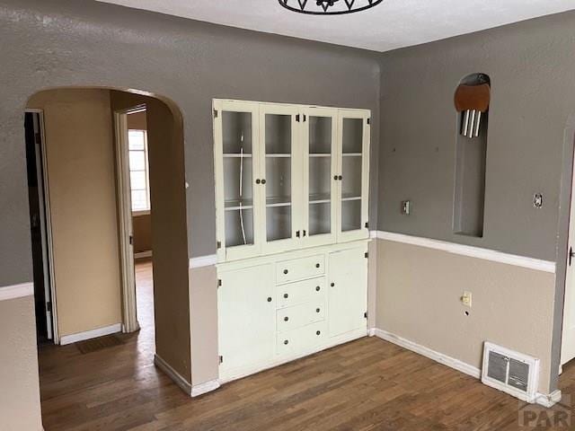 unfurnished dining area featuring baseboards, visible vents, arched walkways, and dark wood-style flooring