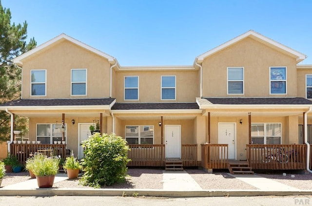 townhome / multi-family property featuring a porch, roof with shingles, and stucco siding