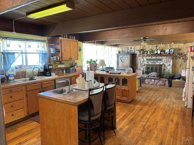 kitchen featuring a fireplace, tile countertops, brown cabinetry, a sink, and beamed ceiling