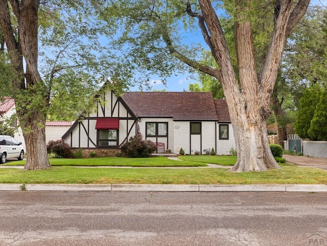 english style home with stucco siding, a shingled roof, and a front yard