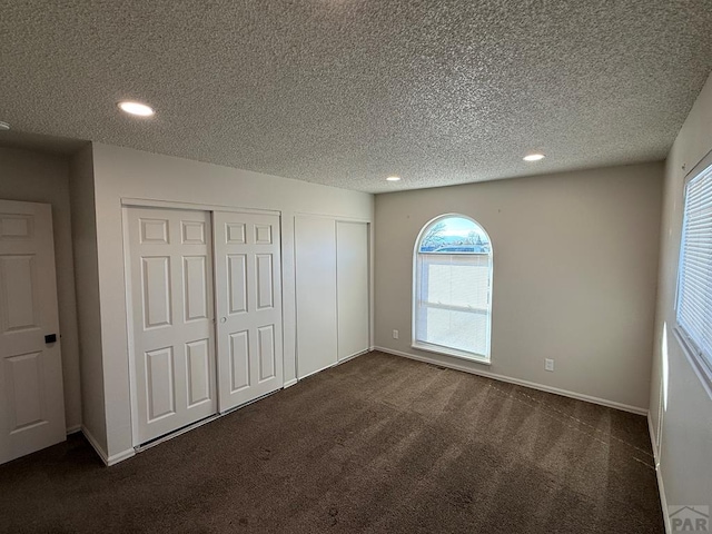 unfurnished bedroom with baseboards, dark colored carpet, a textured ceiling, two closets, and recessed lighting