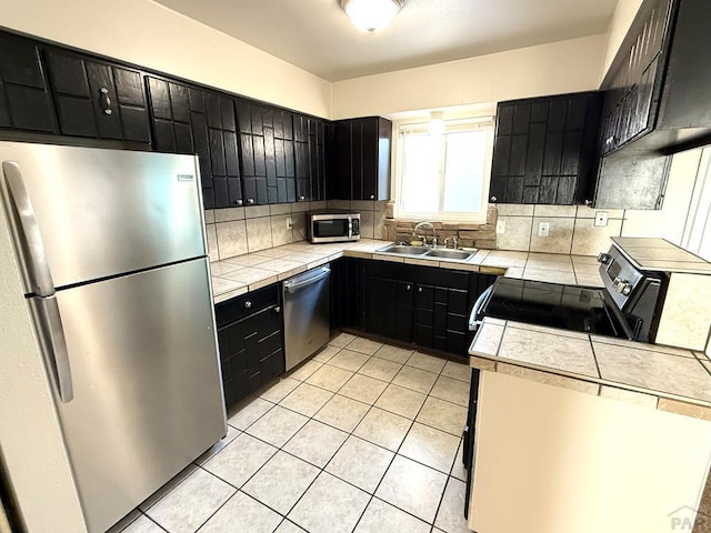 kitchen with tasteful backsplash, tile countertops, stainless steel appliances, dark cabinetry, and a sink