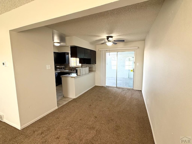 kitchen featuring a ceiling fan, light colored carpet, stainless steel microwave, a textured ceiling, and dark cabinetry