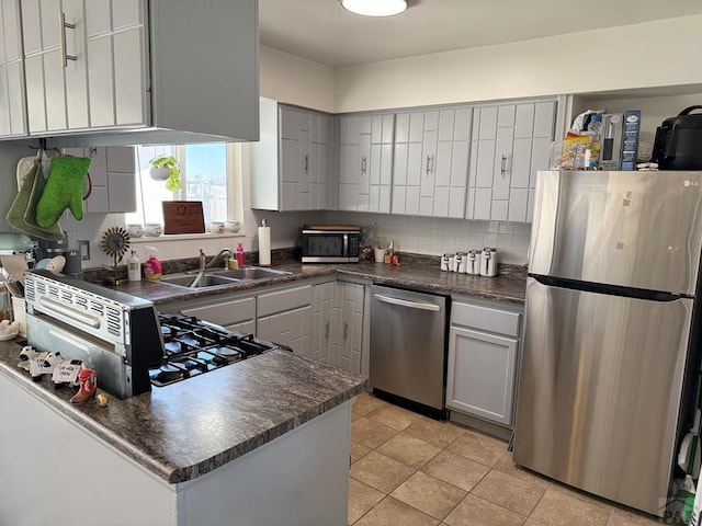 kitchen featuring tasteful backsplash, dark countertops, appliances with stainless steel finishes, gray cabinetry, and a sink