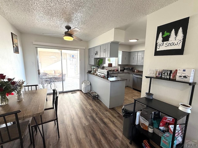 kitchen with dark countertops, gray cabinetry, wood finished floors, dishwasher, and a peninsula