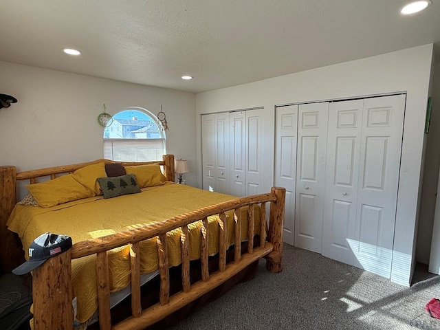 bedroom featuring a textured ceiling, dark colored carpet, two closets, and recessed lighting