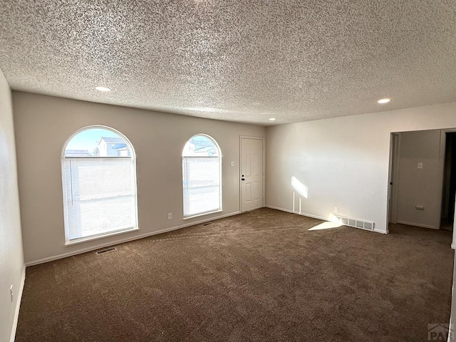 empty room with baseboards, visible vents, dark colored carpet, and a textured ceiling